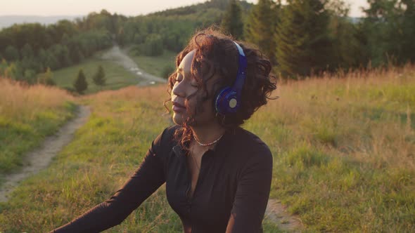 Portrait of Calm Pretty Black Female in Headphones Meditating on Mountain Peak at Dawn alt