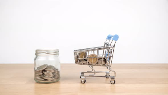 Stop motion animation shopping cart are carrying coins into a clear glass jar on wooden desk