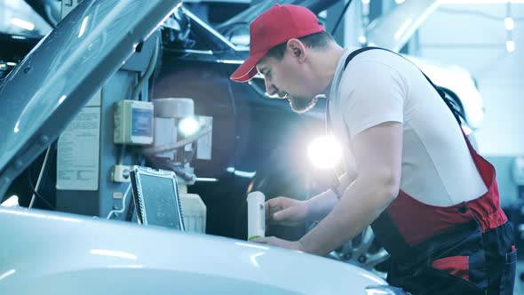 Car Repair Master Conducts a Diagnostics Test Using a Laptop and a Flashlight alt