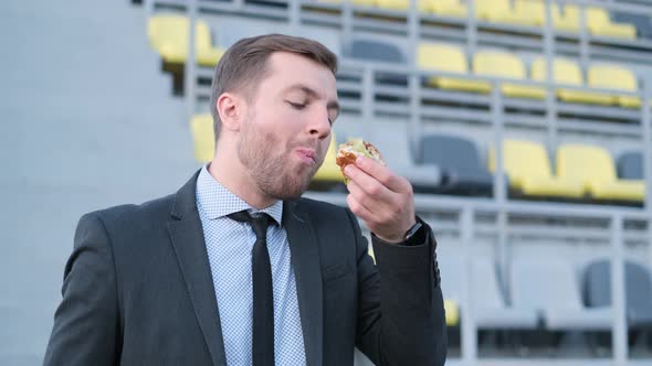 A Young European Man Eating a Takeaway Coffee Sandwich Next to Him During a Lunch Break on a City alt