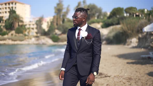 Portrait of Thoughtful Lonely African American Groom in Elegant Suit Strolling on Sandy Beach in alt