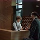Male Guest Talking To Hotel Receptionist and Getting Key Card While Man and Woman Walking By