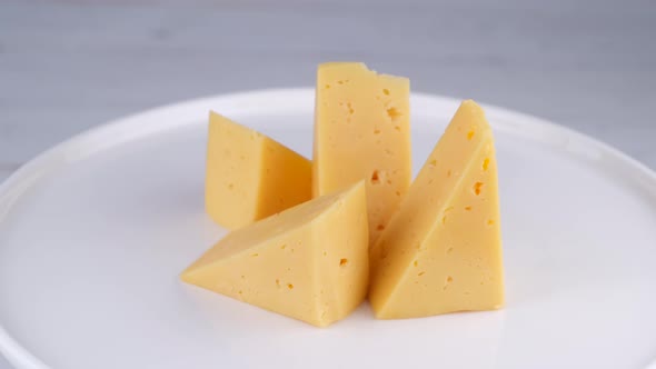 Rotating Pieces of Hard Cheese on a White Plate or Background Closeup