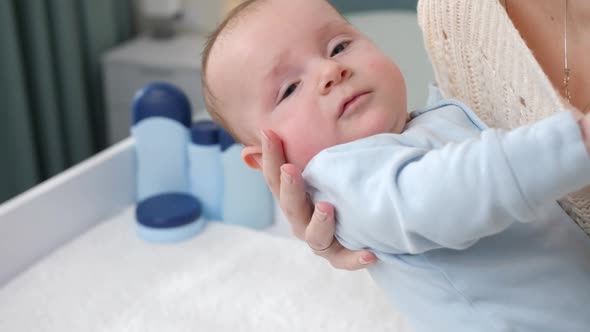 Closeup of Young Caring Mother Laying Her Little Baby Son on Dressing Table alt