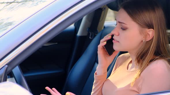 Young Upset Woman is Talking on the Phone While Driving a Standing Car alt