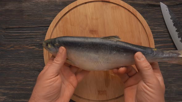 Top View of Hands Starting to Peel the Red Char Fish on the Round Wooden Board alt