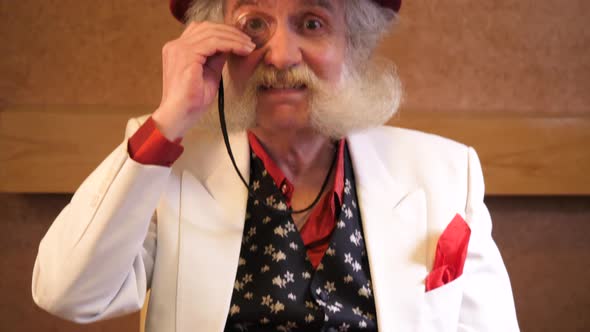 Older man with stylish beard puts in monocle and gives a thumbs up to camera alt