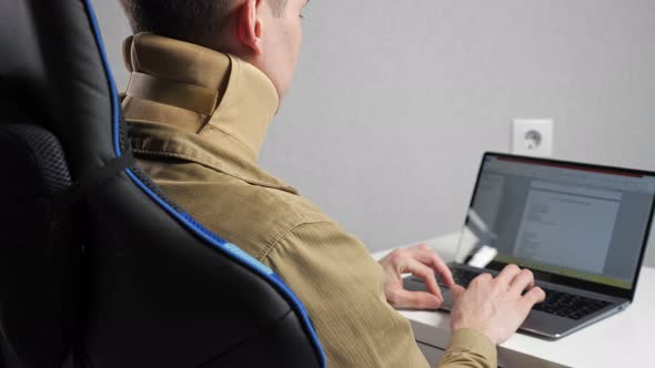 Man with Bandage on Neck Works with Document in Laptop at Table