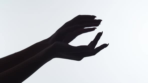 Closeup of the silhouette of woman's hands on white background, runs finger along arm after applying alt