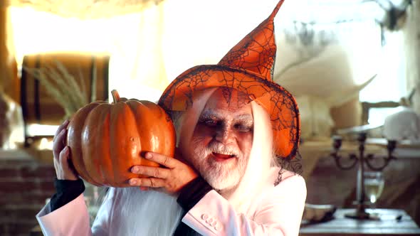 Halloween Old Man with Pumpkin in Hand. Bearded Man Ready for Halloween Party. Evil Wizard Hold alt