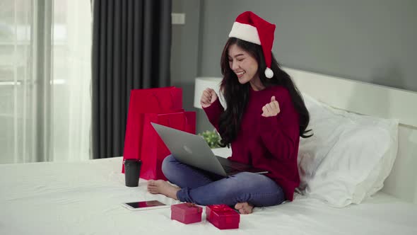 happy woman shopping online for Christmas gift with computer laptop and credit card on a bed