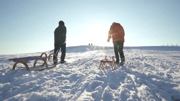 Active Seniors Walking up Hill With Winter Sledges alt