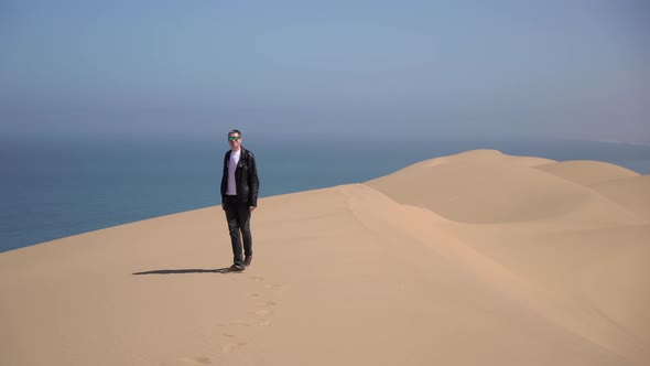A Young Man Walks Along Sandy Dunes on the Seashore