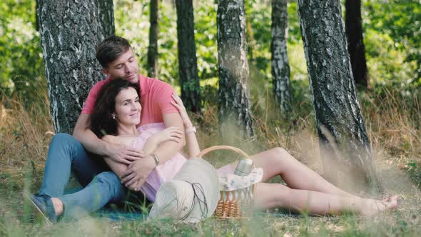 Picnic Time. Happy Young Couple Having Fun. The Man Hugs His Girlfriend and Strokes Her Hands alt