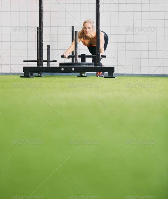Fit young female using prowler exercise equipment at gym Stock Photo by
