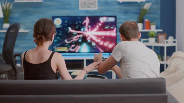 Couple Arguing Over Man Losing Online Game on Console in Front of Big Screen Tv alt