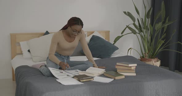 Black Female Student Studying with Books in Bed alt