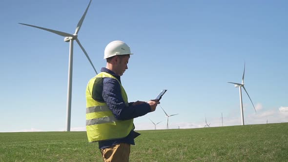 Technician Standing Near Wind Mill and Monitoring System on Tabl alt