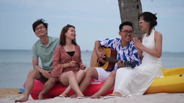 Group of friends having fun on the beach with a guitar and singing songs