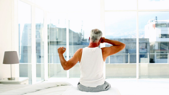 Mature Man Yawning And Stretching Sitting On Bed