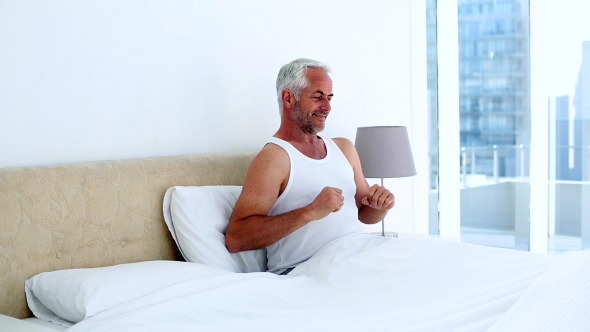 Smiling Man Yawning And Stretching Sitting On Bed