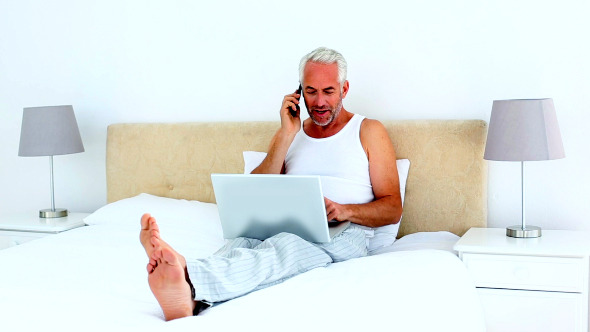 Smiling Man Using Laptop While On The Phone