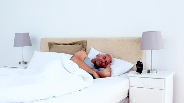 Refreshed Man Waking Up And Looking At Alarm Clock