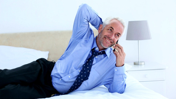 Businessman Talking On The Phone Lying On His Bed