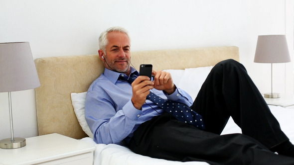 Businessman Lying On His Bed Listening To Music