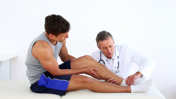 Mature Doctor Touching Sportsmans Injured Ankle
