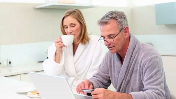 Mature Smiling Couple Shopping Online At Breakfast