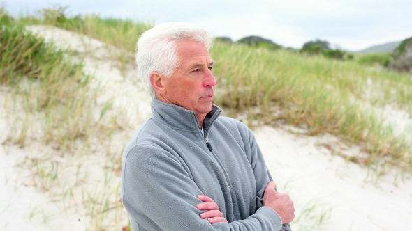 Retired Man Standing On The Beach Shivering