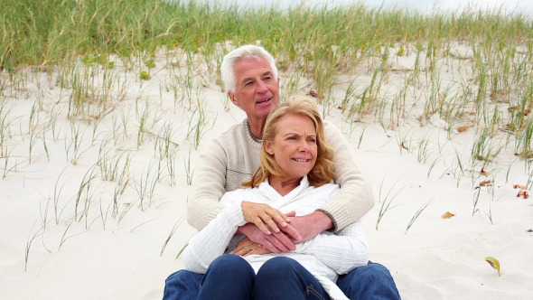 Smiling Retired Couple Sitting On The Beach