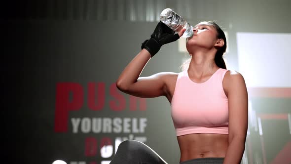 Fitness women take a break and drink water inside the gym.