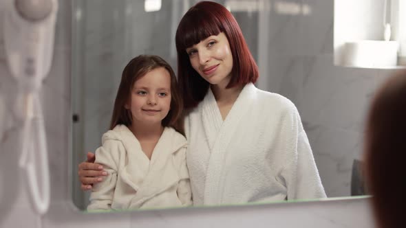Mother and Daughter in White Bathrobes Standing in the Bathroom During the Morning Procedures alt