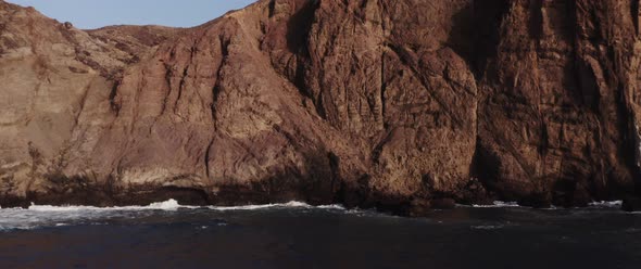 Drone shot of a rocky mountain by the wavy sea alt