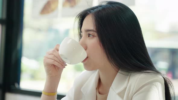 beautiful Asian woman is sitting comfortably sipping coffee in a cafe.