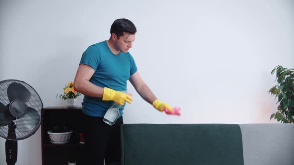 A man cleans the sofa in the room with a rag and a cleaning agent, close-up
