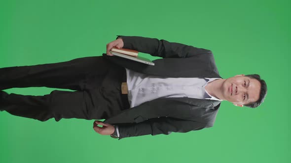 Asian Business Man Holding Book And Laptop While Walking On Green Screen Chroma Key alt