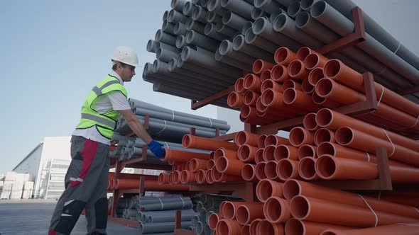 Wide Shot Storage of Plastic Pipes Outdoors with Caucasian Male Worker Entering Taking One and alt