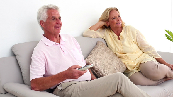 Retired Smiling Couple Watching Television On The