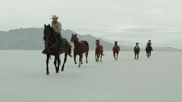 Horses running with cowboys riding across salt flats. alt