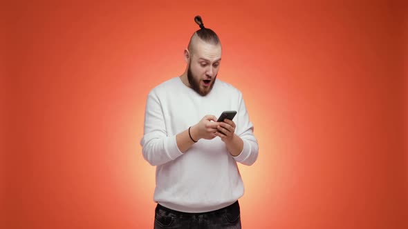 Overjoyed Young Bearded Man Is Looking on Smartphone Doing Winner Gesture alt
