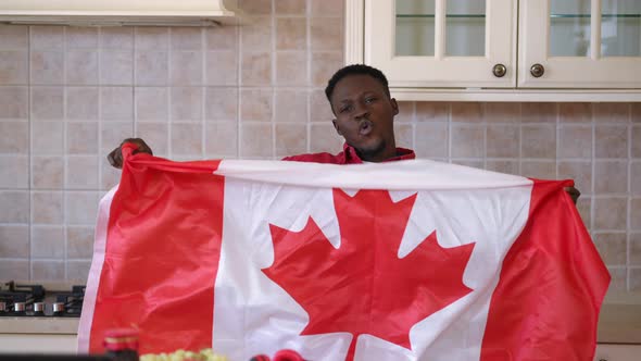 Front View Positive African American Man Shacking Canadian Flag Posing in Kitchen Indoors alt