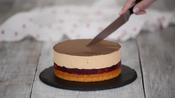 Woman Cuts a Piece of Homemade Cherry Cake with Caramel Mousse and Sponge Cake Layer