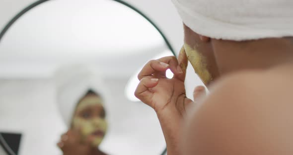 Happy african american woman apply beauty mask on face in bathroom alt