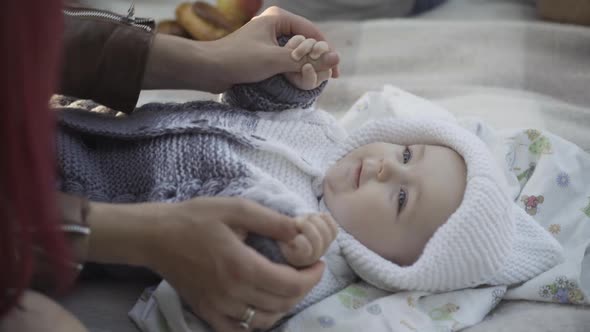 Unrecognizable Young Caucasian Woman Playing with Cute Infant Lying on Blanket Outdoors alt