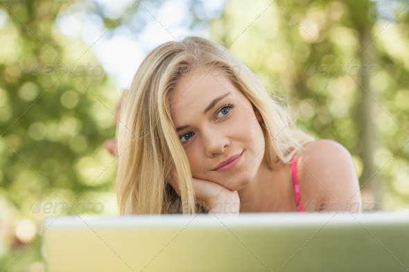 Day dreaming attractive woman lying in front of her notebook on a lawn