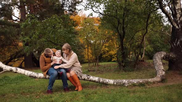 Young Parents Walking with Daughter in Forest in Autumn