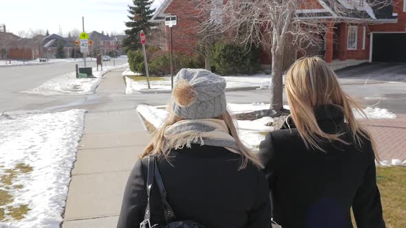 Two Young Females Walking Up To An Intersection Talking In Winter From Behind